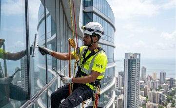 Rope access window cleaner washing glass facade on high-rise office skyscraper.